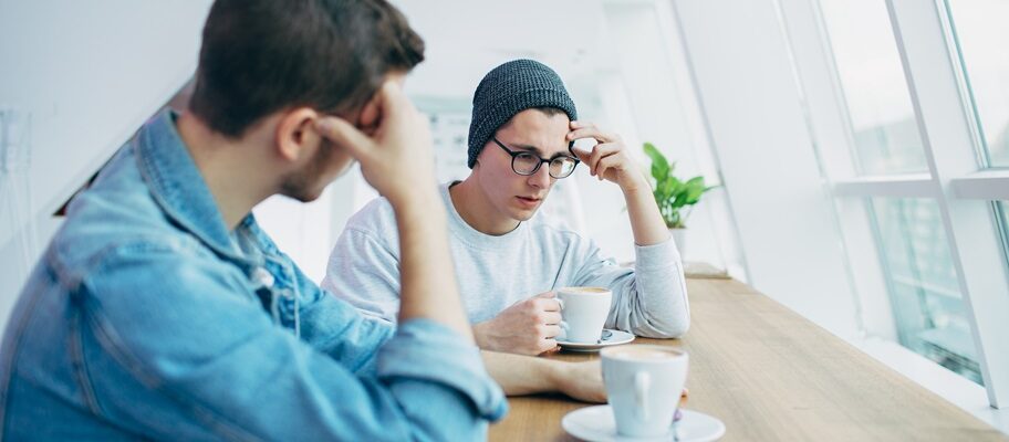 Två unga män i samtal över en kaffe, ser ut att prata om något tungt.