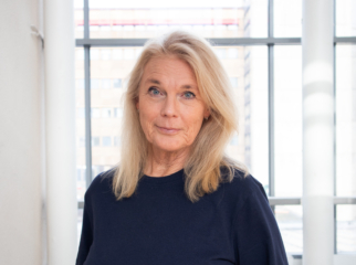 Lolo Westerman med blont, axellångt hår och mörk tröja framför fönster