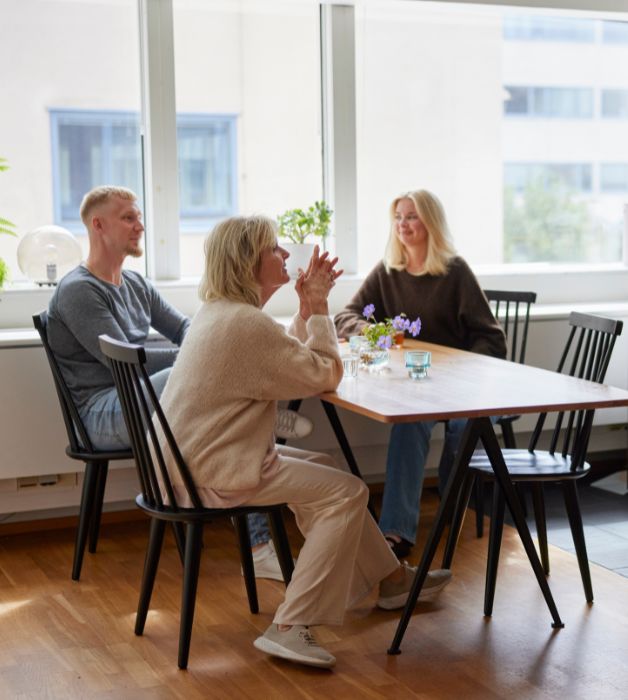 Tre volontärer sitter tillsammans i ett kök. De ler mot varandra i en ljus miljö som känns hoppfull.