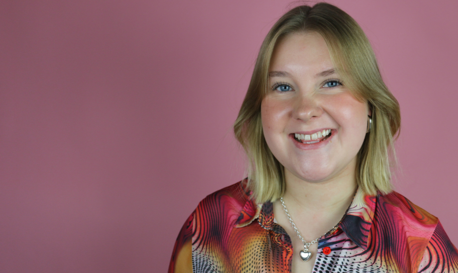 Internetprofilen Beatrice Reiman står framför en rosa vägg iklädd en färgglad skjorta. Hon tittar in i kameran och ler.