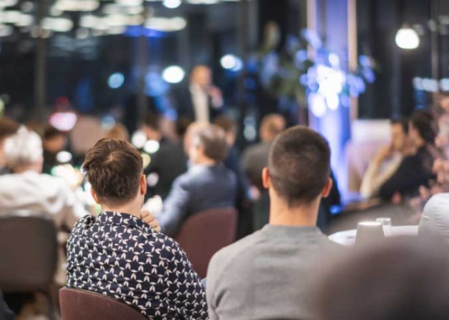 Konferenssal med personer fotograferade bakifrån