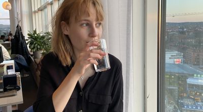 Ellen Nilses, redaktör för Mind Unga, dricker vatten och ser ut genom fönstret. Utsikt över stadslandskap.