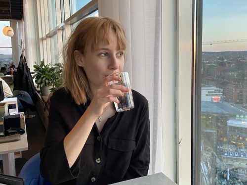 Ellen Nilses, redaktör för Mind Unga, dricker vatten och ser ut genom fönstret. Utsikt över stadslandskap.