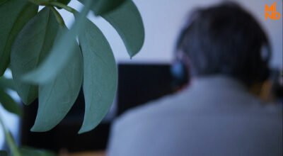 Ryggen av en volontär med headset framför datorn, gröna blad i förgrunden.